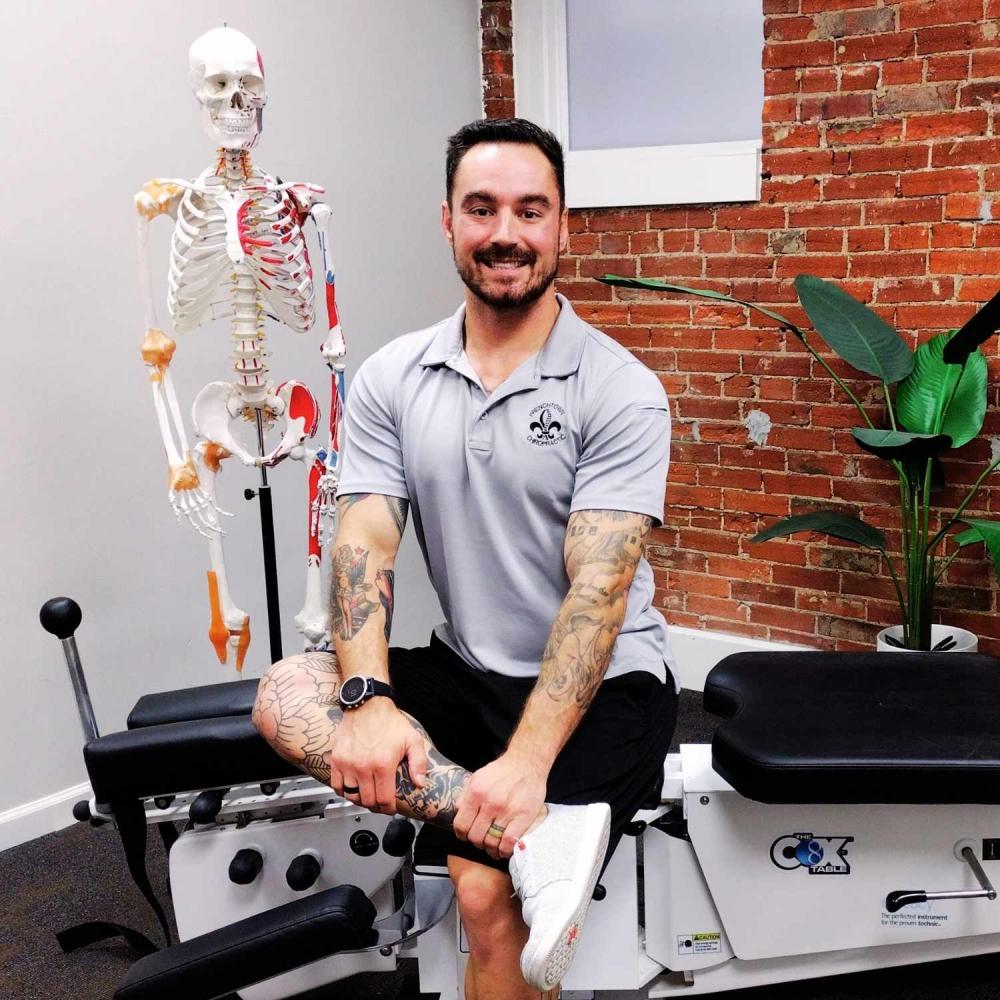 Photo of Dr. Kevin Pisle, Chiropractor smiling and sitting on his adjustment table