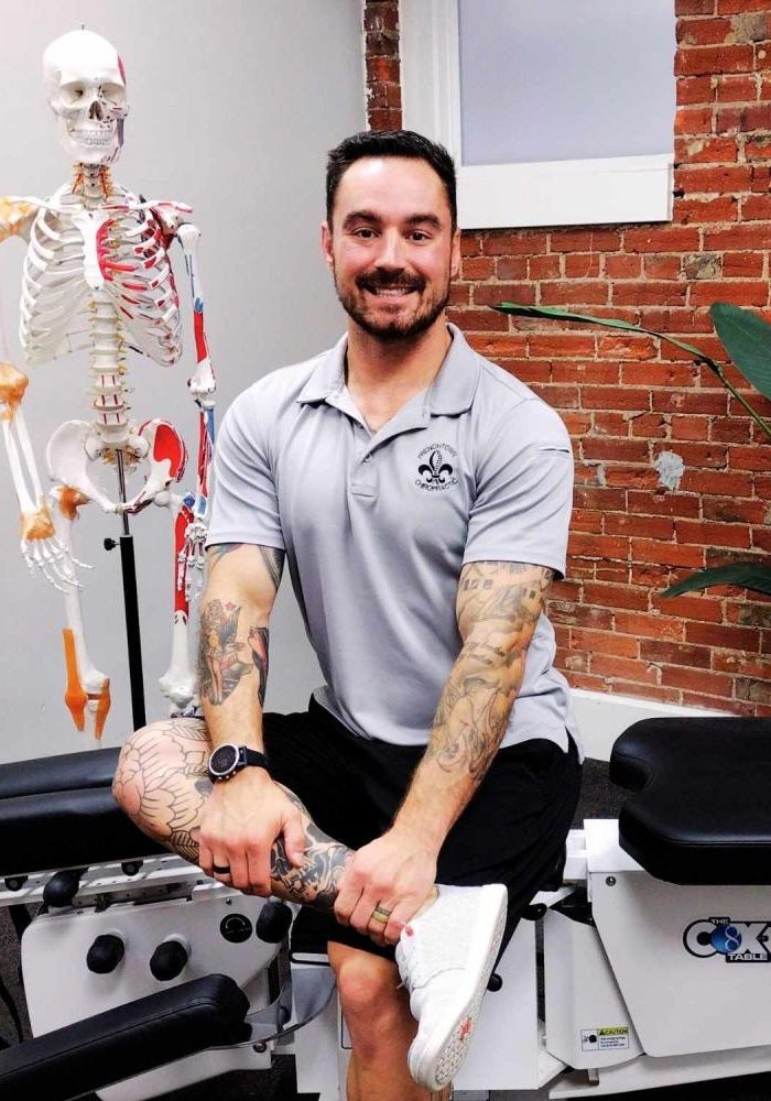 Photo of Dr. Kevin Pisle, Chiropractor smiling and sitting on his adjustment table