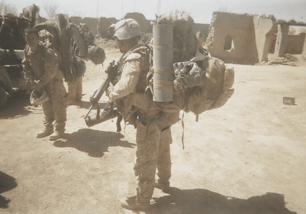 A photo of Dr Kevin Pisle on active duty during his Marine Corps. He is dressed in camouflage with a heavy load of equipment on his back — the beginning of his back problems.
